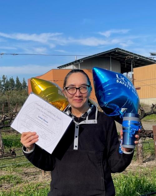 woman standing with two balloons and coffee cup with Safety Star Award certificate for Leticia Rodriguez
