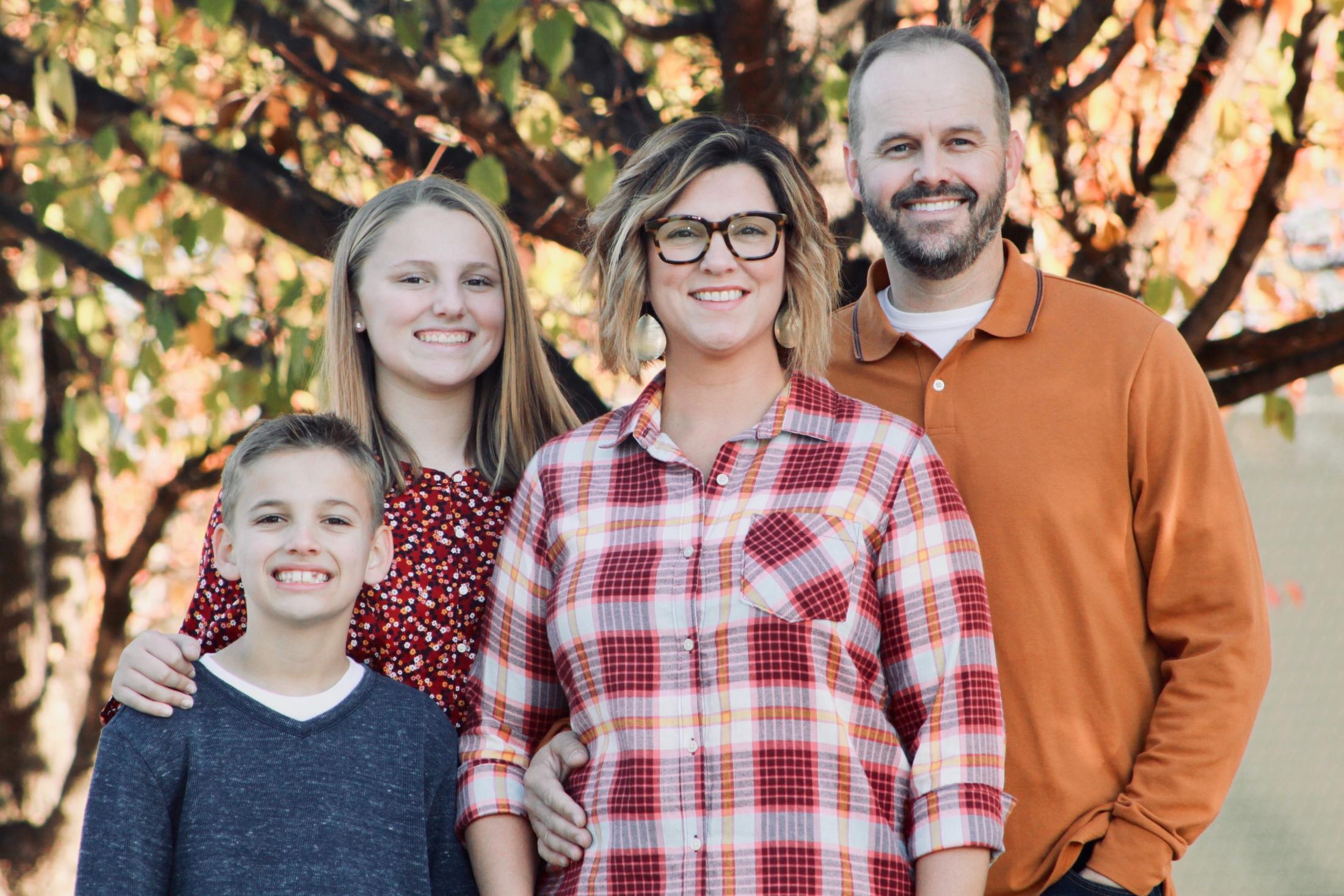 Family of four with daughter and son standing in front of tree