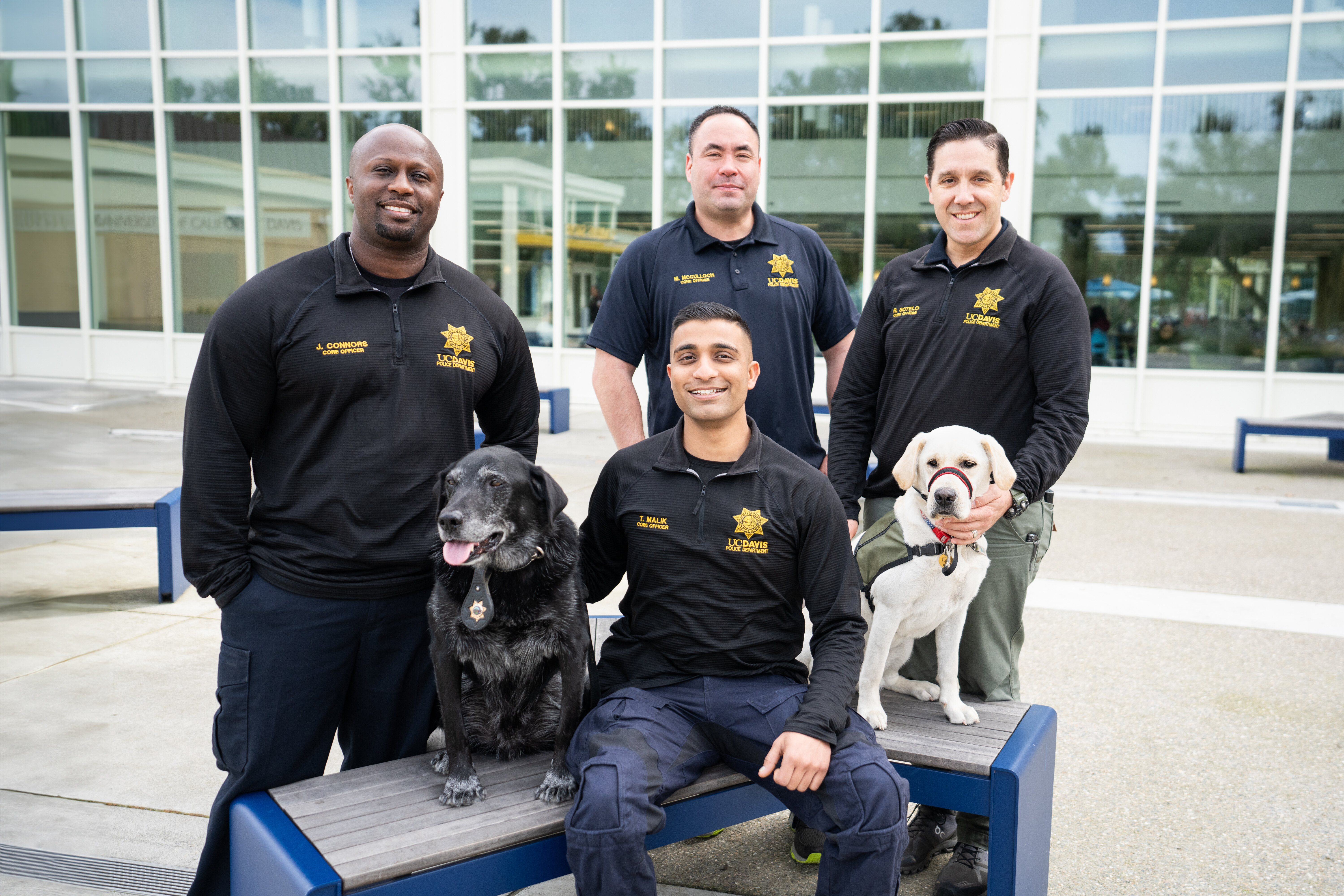 CORE Officers in uniform and their two dogs sit and smile outside the MU.