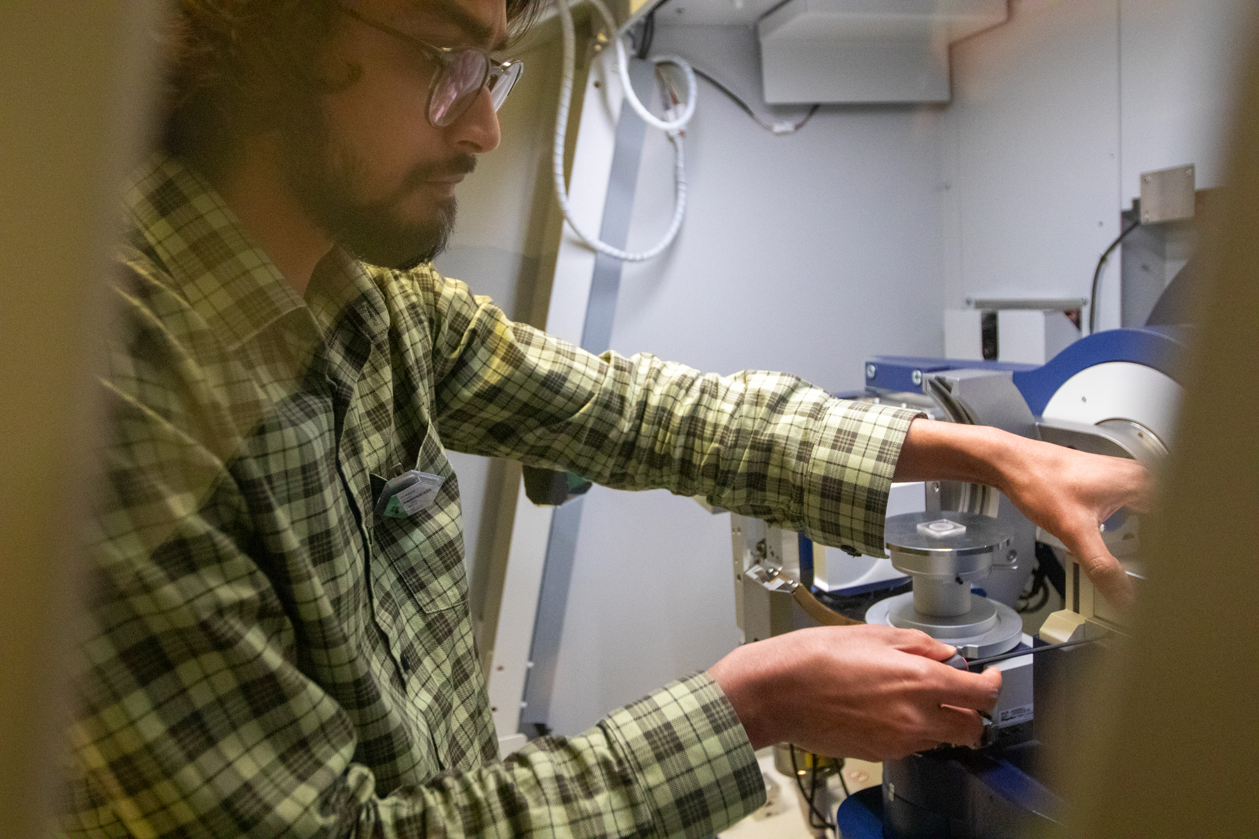 A man in a checkered green shirt operates a machine.