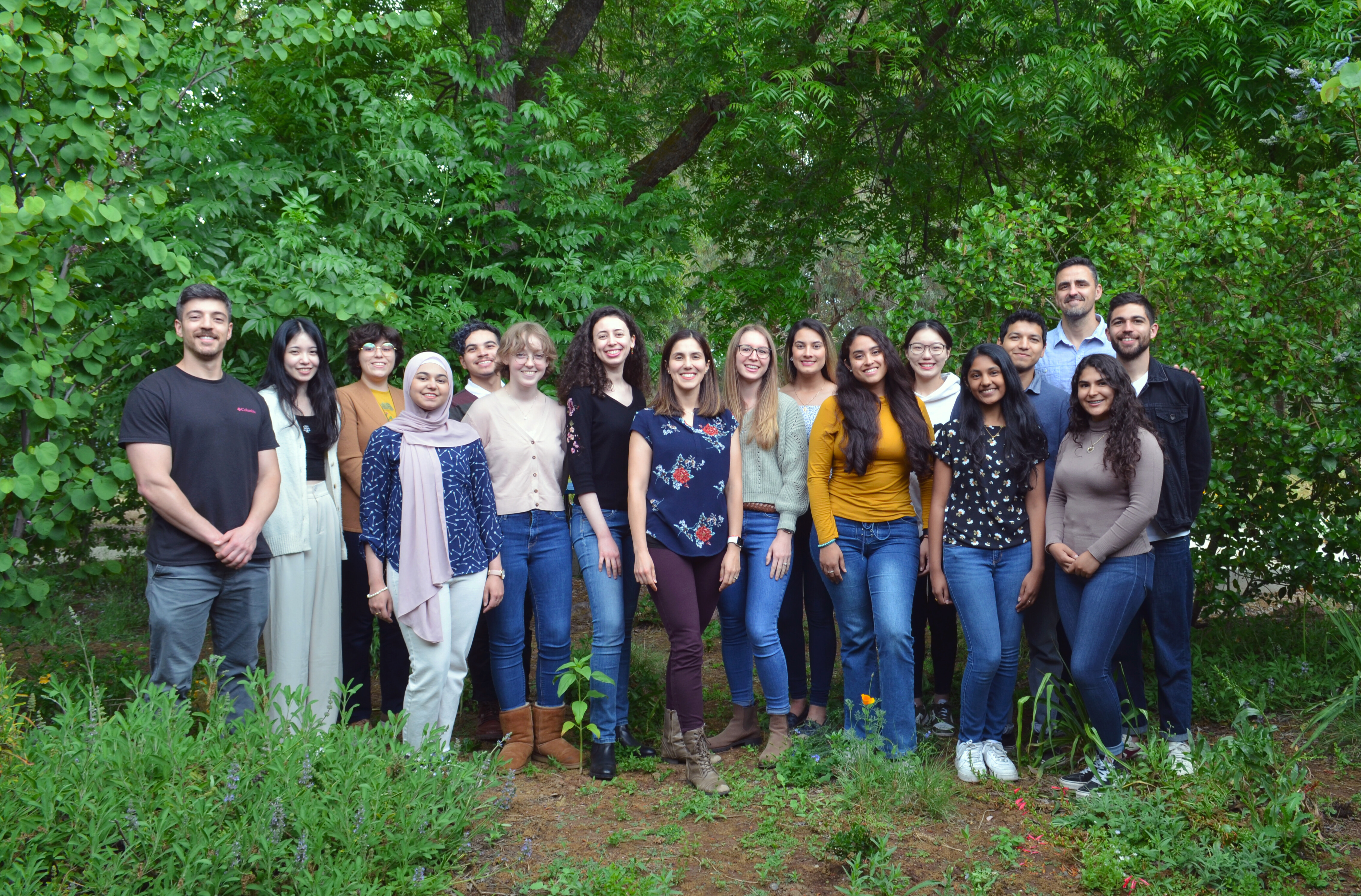 Dr. Bárbara Blanco-Ulate (center) and her lab group standing together and smiling in front of some trees.