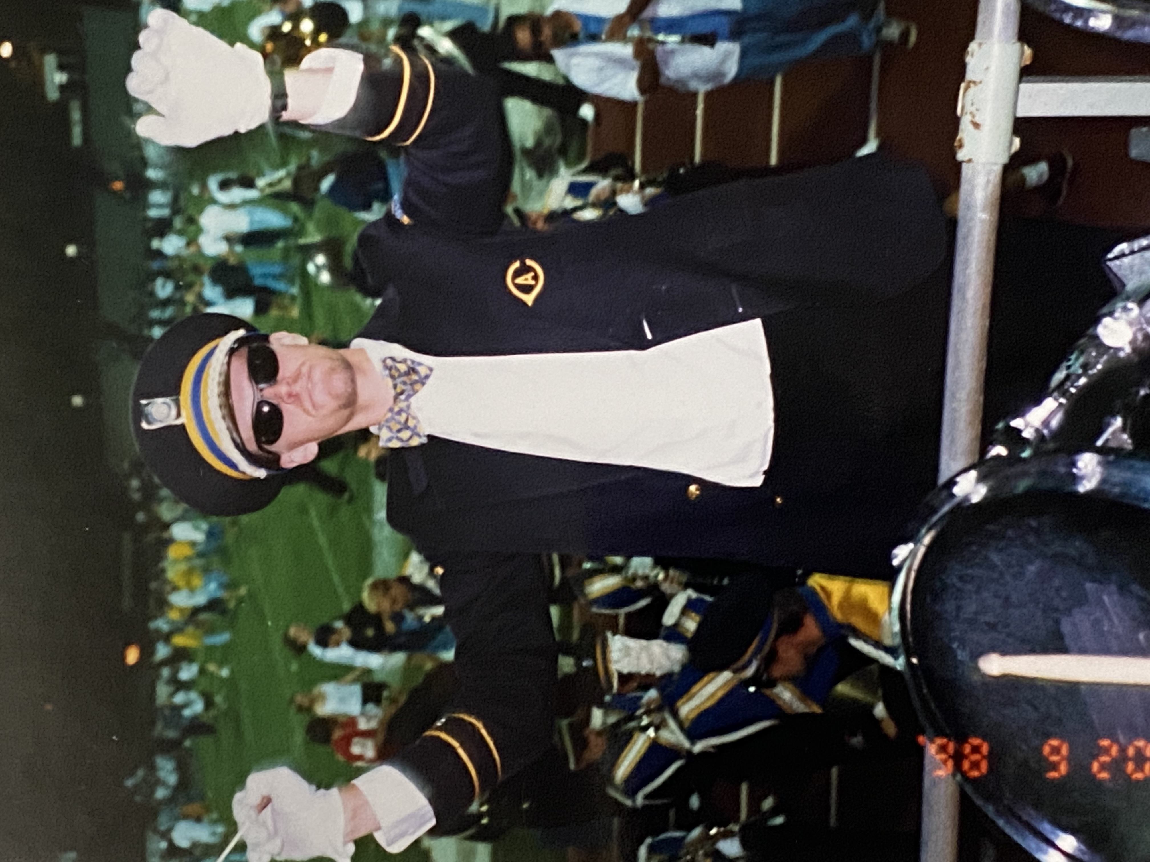 Student in marching band uniform conducting  in front of field