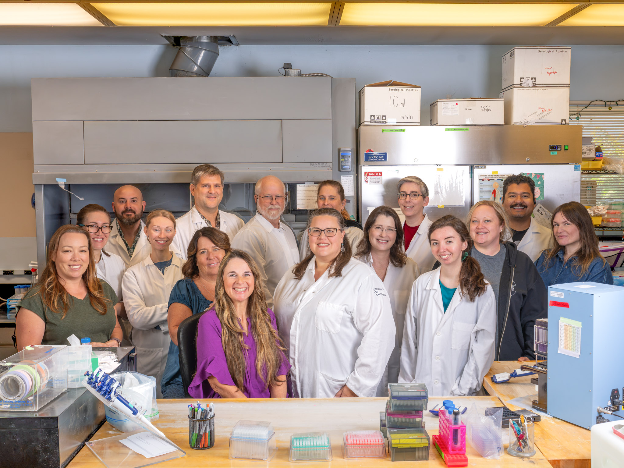 Group of scientists in lab coats smiling behind a laboratory bench in the UC Davis VGL