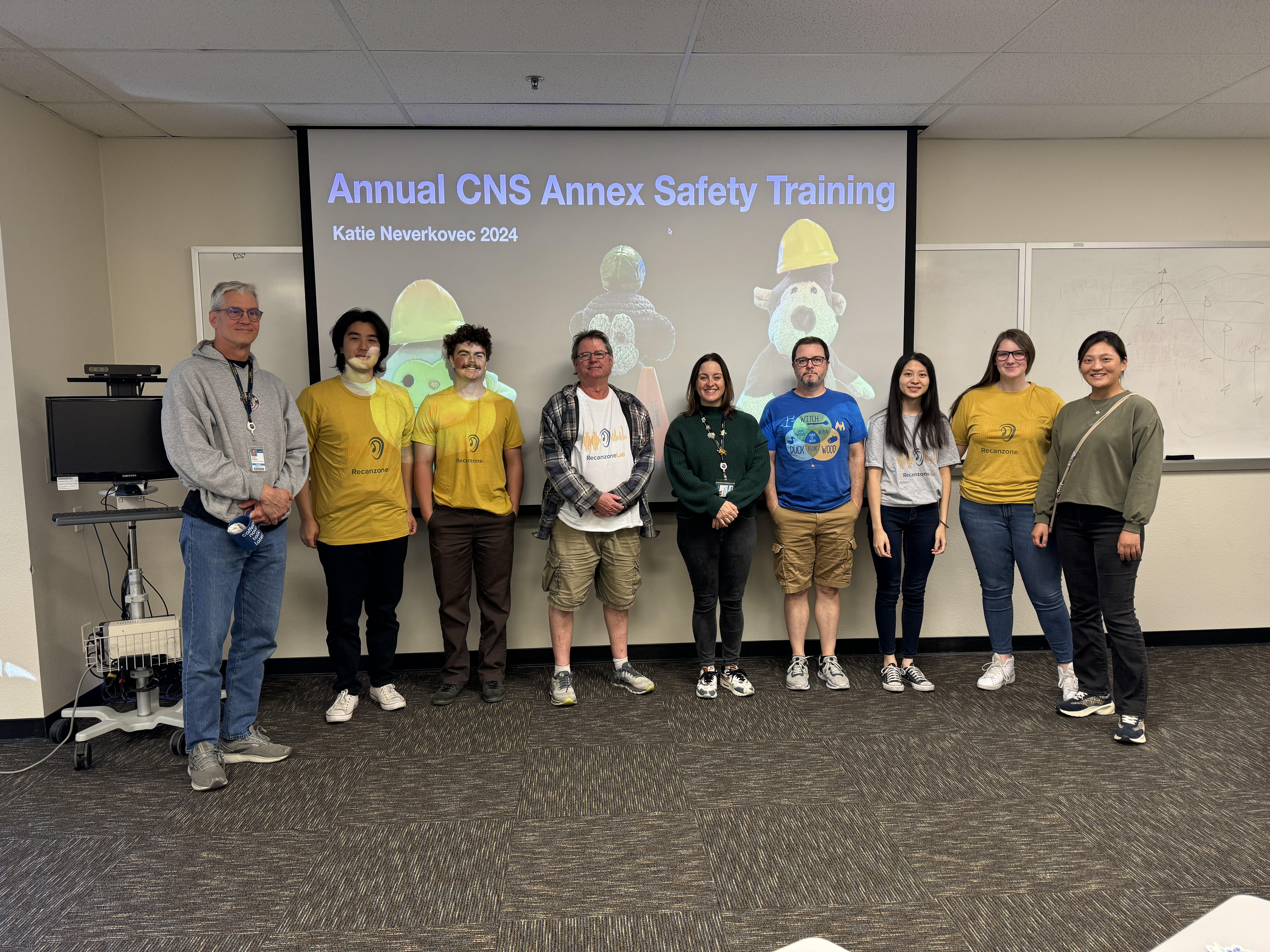 Dr. Gregg Recanzone and his lab members stand and smile in front of a powerpoint that reads "Annual CNS Safety Training."