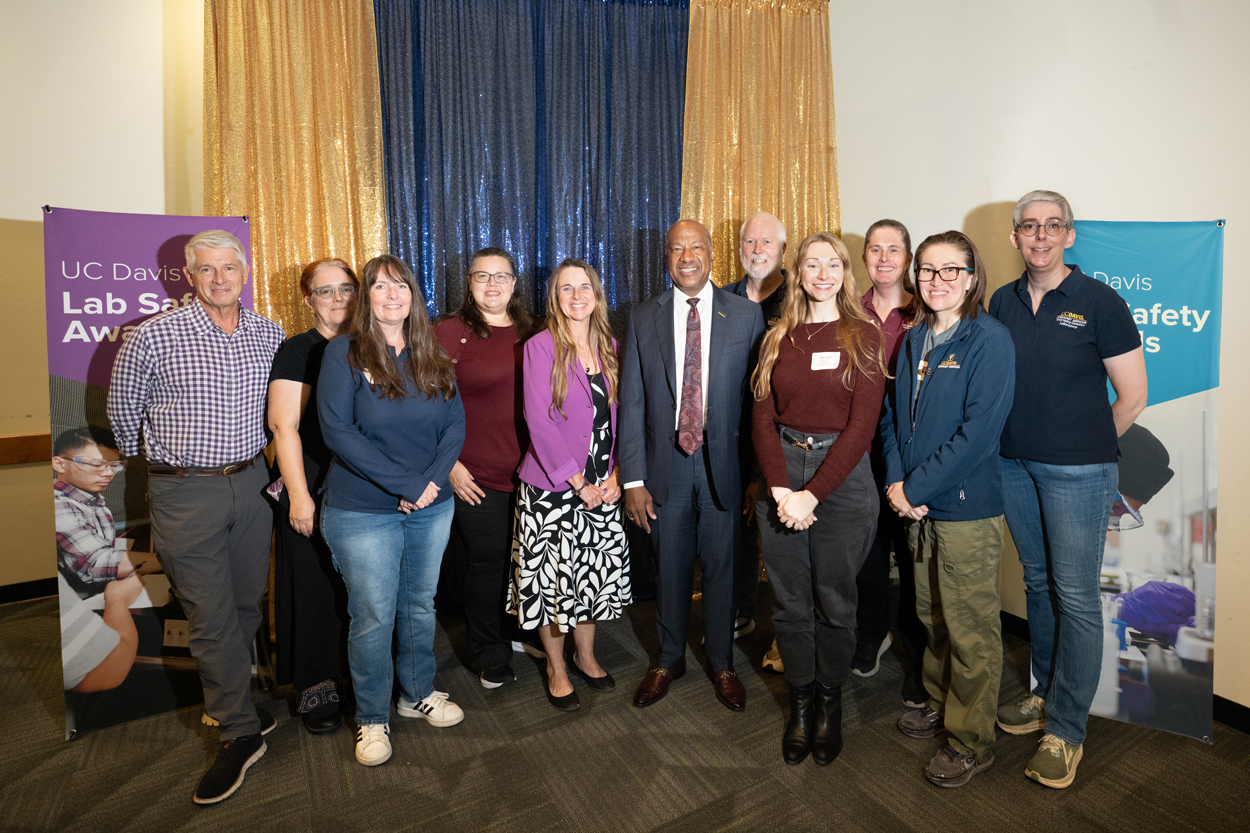 Group portrait of diverse adults at an indoor event with banners and blue-gold curtain
