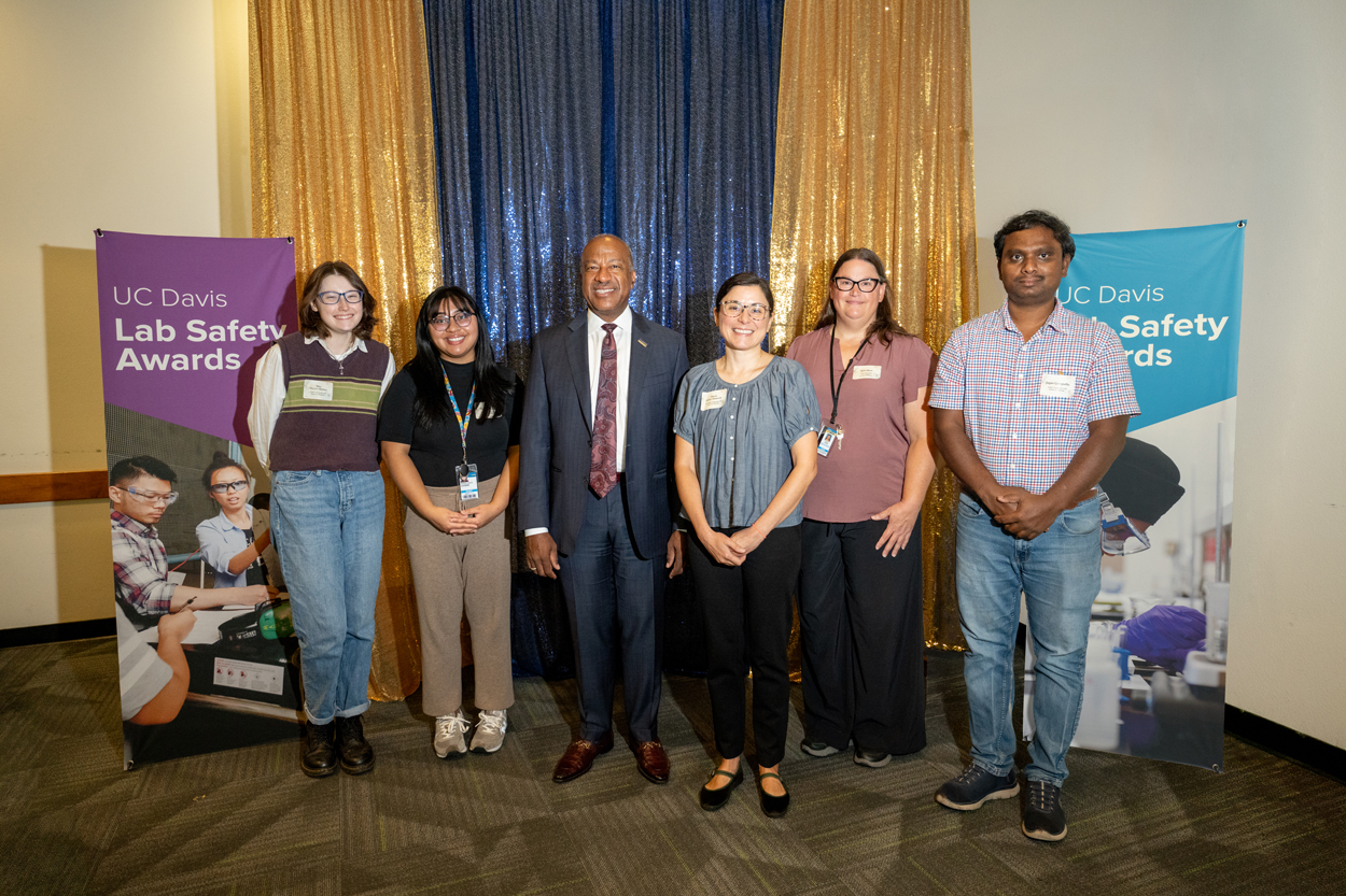 Seven people standing before blue and gold curtains and safety-award banners.