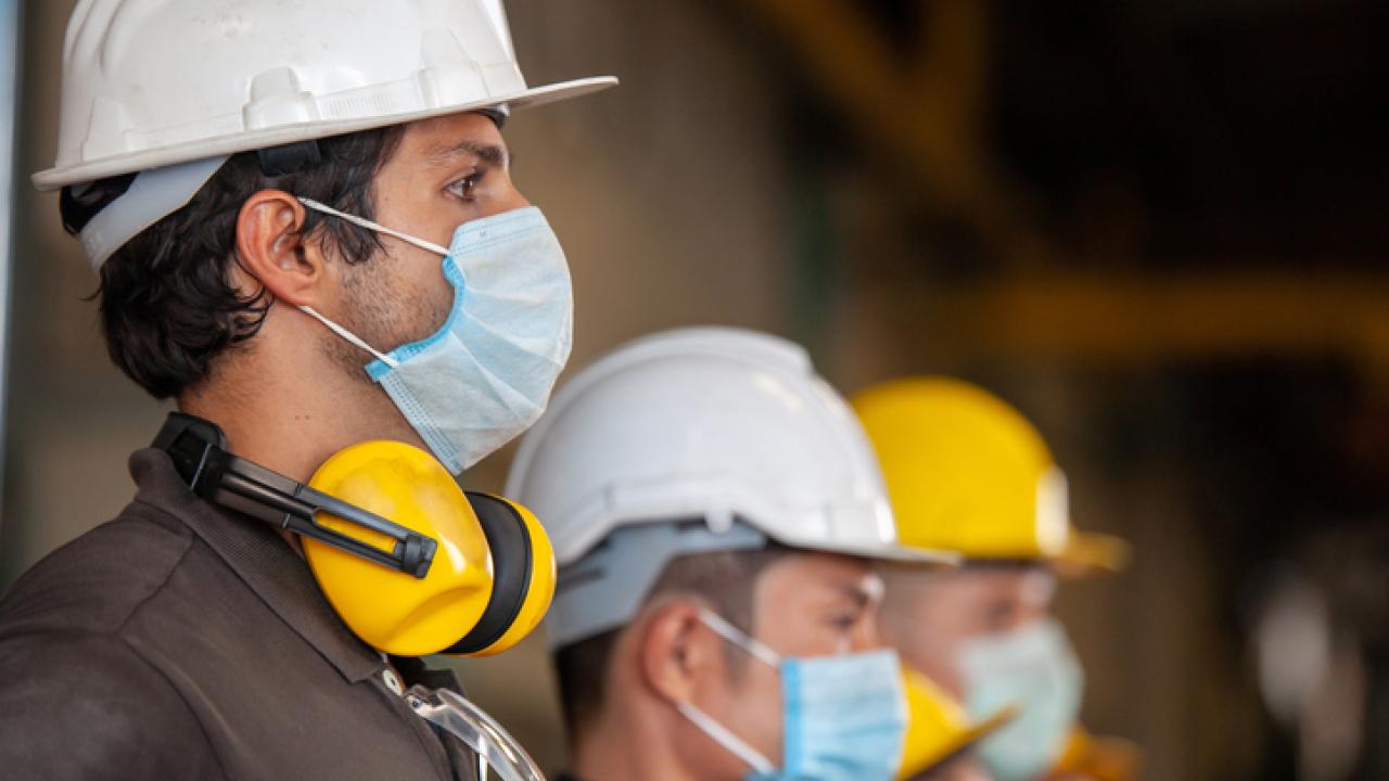 Cal/OSHA employees standing next to each other with helmets and masks on.