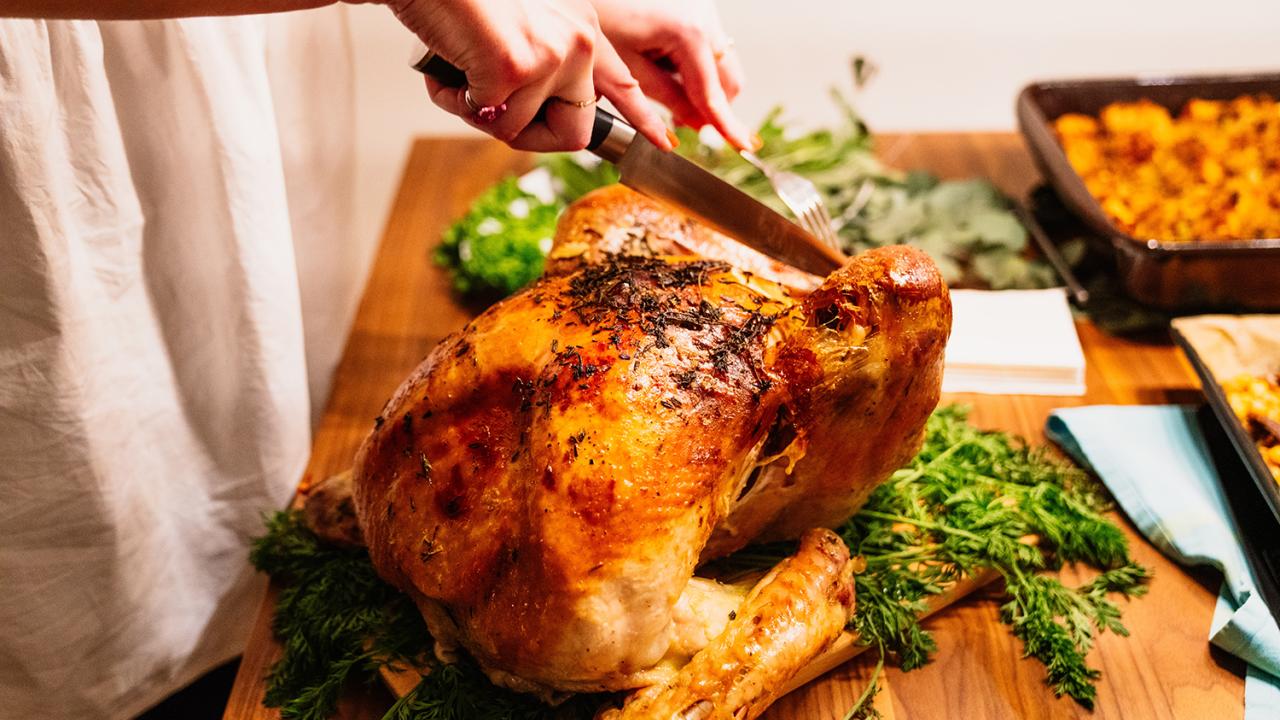 woman carving a cooked turkey at a dinner table