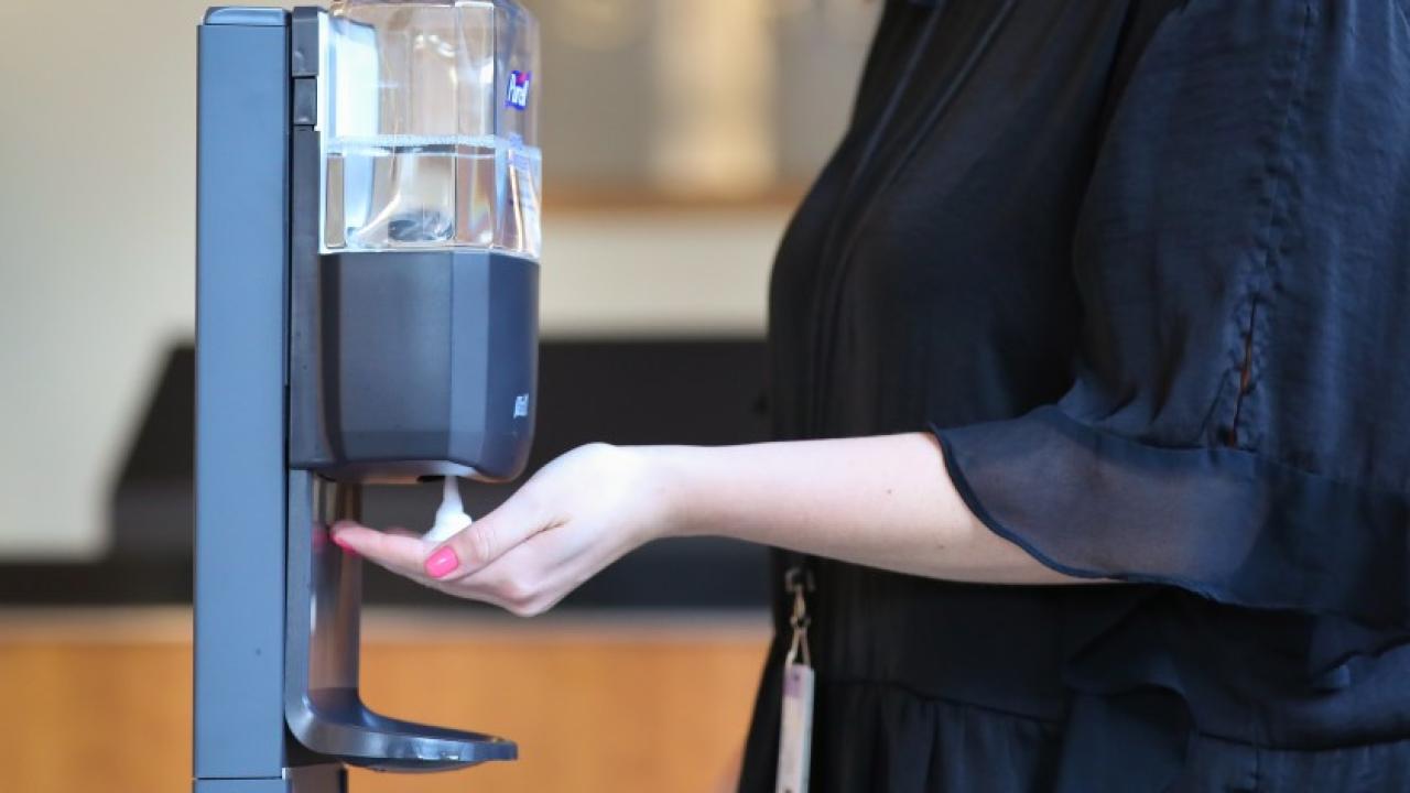person with hand placed under sanitizer dispenser.