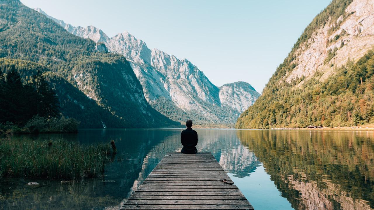 person sitting on a lake dock looking toward mountains