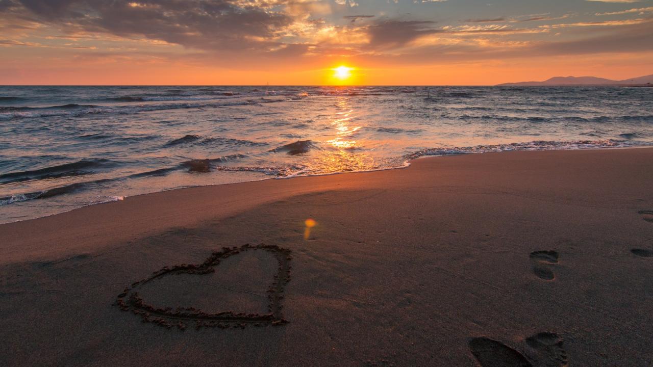 heart shape drawn into sand on a beach at sunset