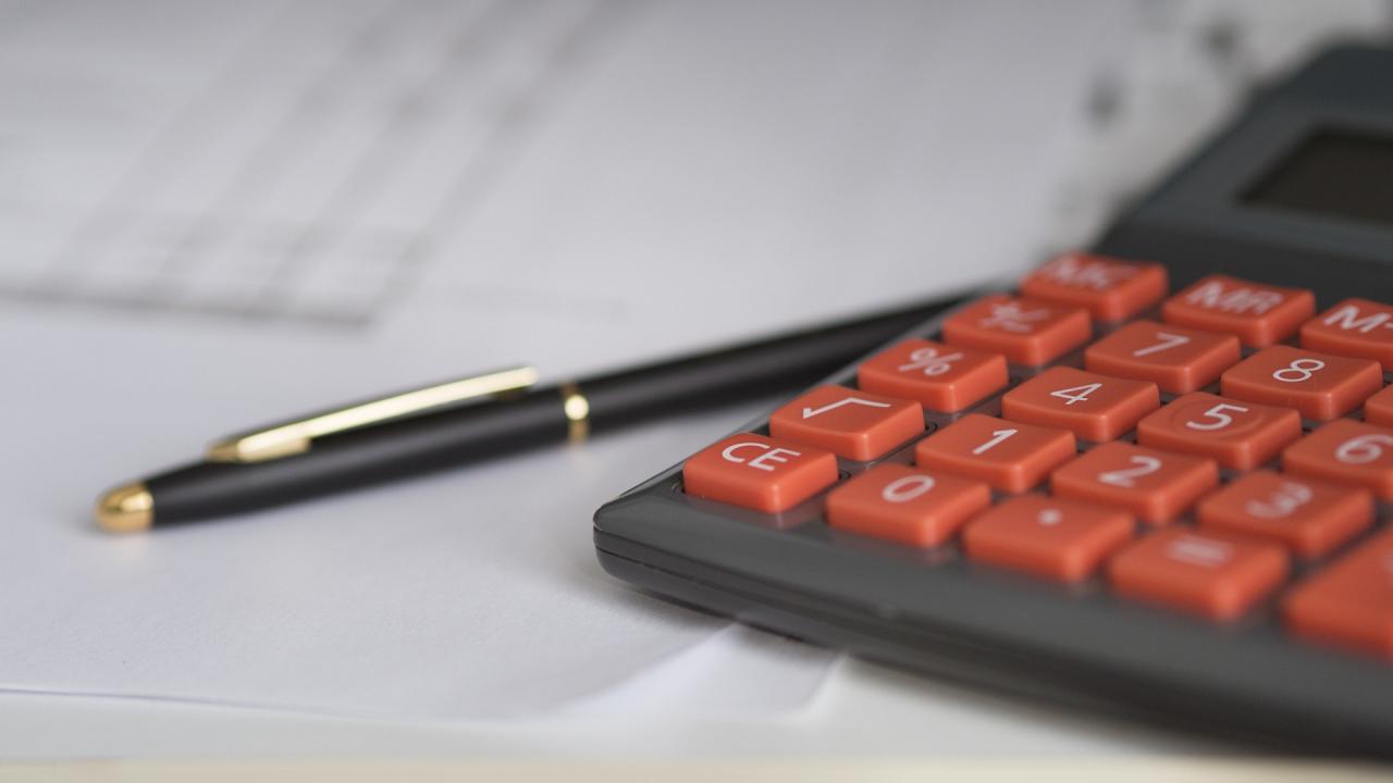 calculator with red buttons, financial paperwork, and a black pen on tabletop