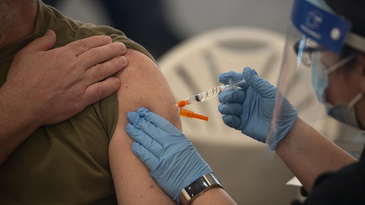 person getting a flu shot in their left arm and holding their right arm in front of their chest