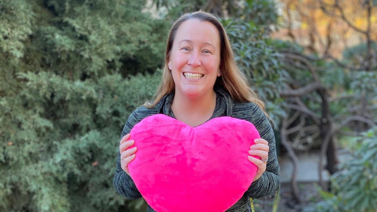 woman holding stuffed heart in front of tree