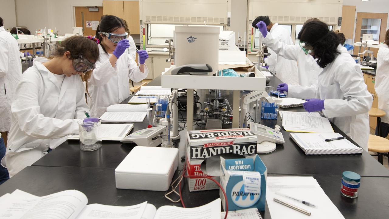 Students in lab coats performing experiments at workstations