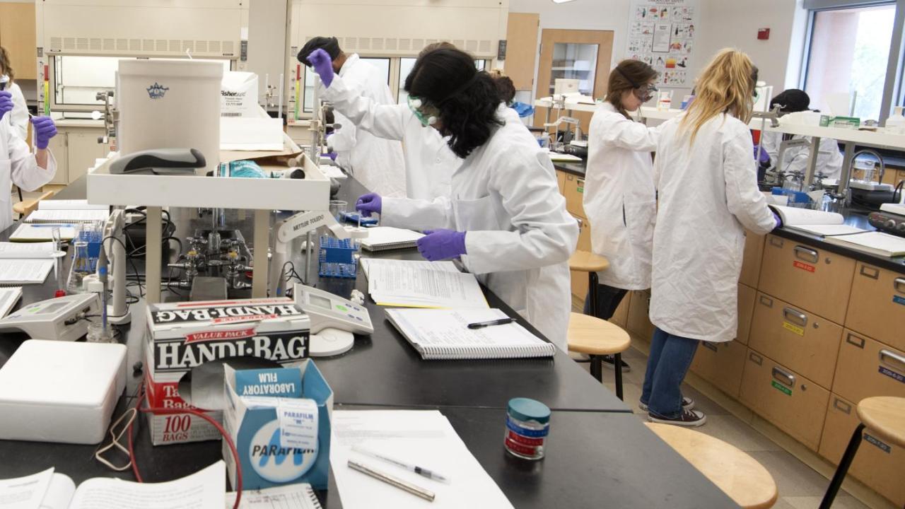 Students in lab coats performing experiments at workstations