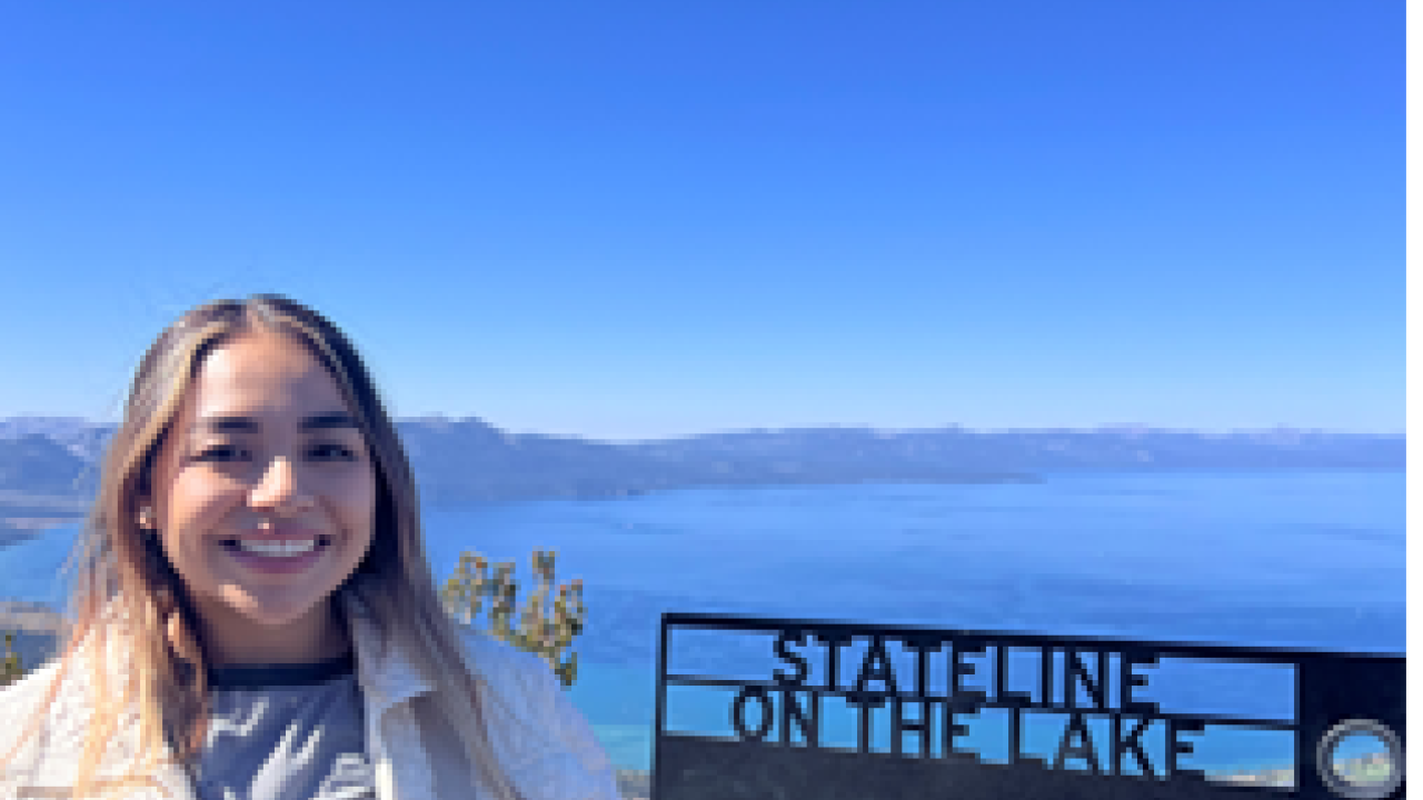 Mayra stands in front of a sea line smiling