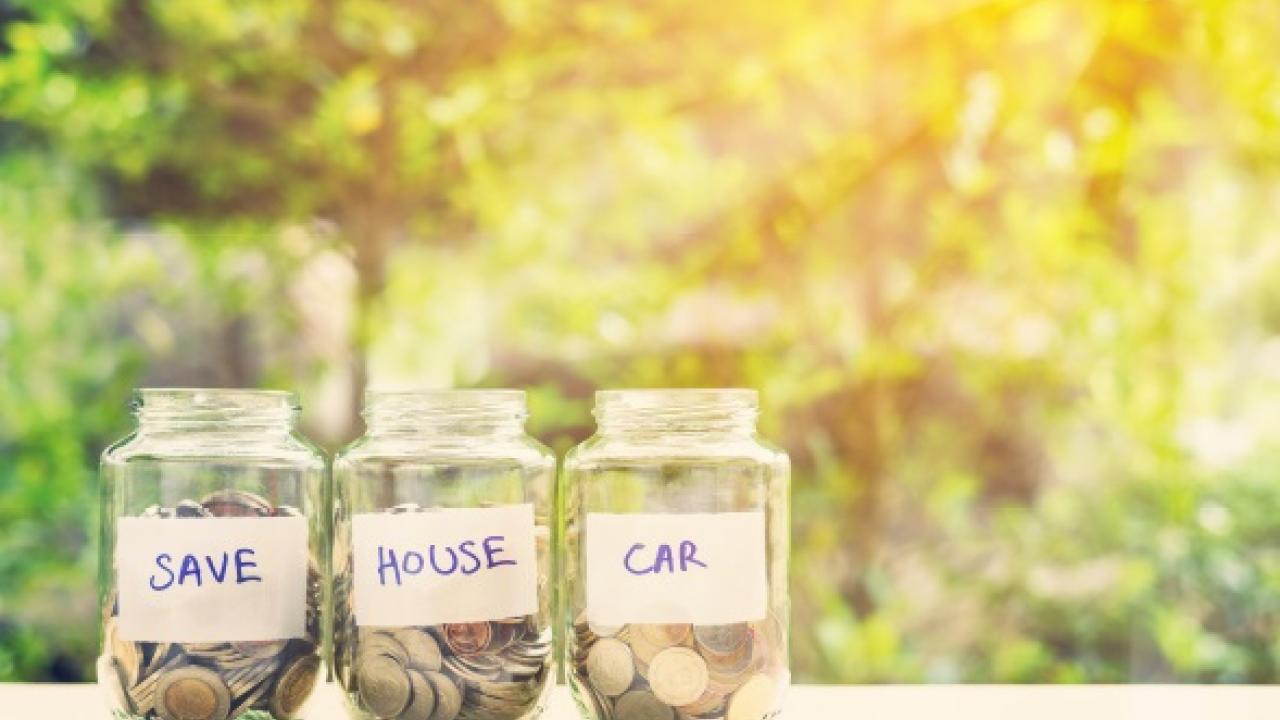 three mason jars filled with coins, one designated for saving, one for a house, and one for a car