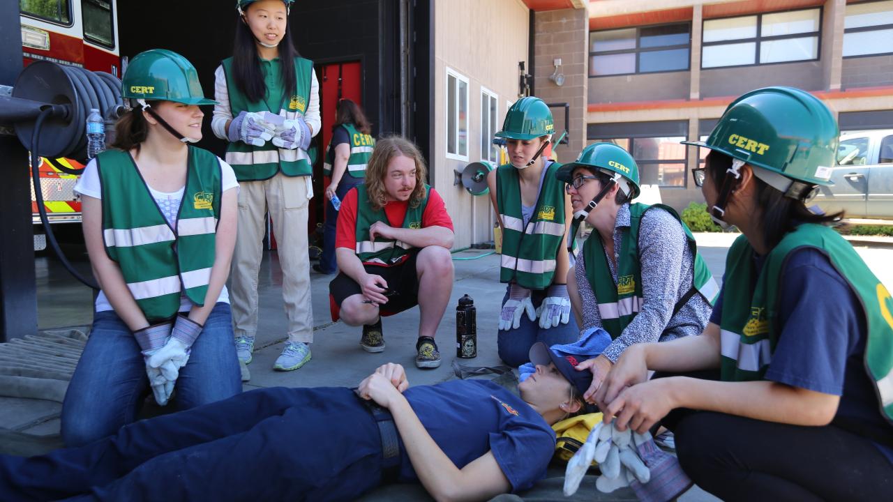 CERT team huddles around a person laying on the floor to practice disaster preparedness