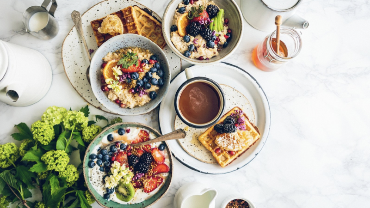 Plates of greens and waffles with bowls of oatmeal and fruit on a white marble counter