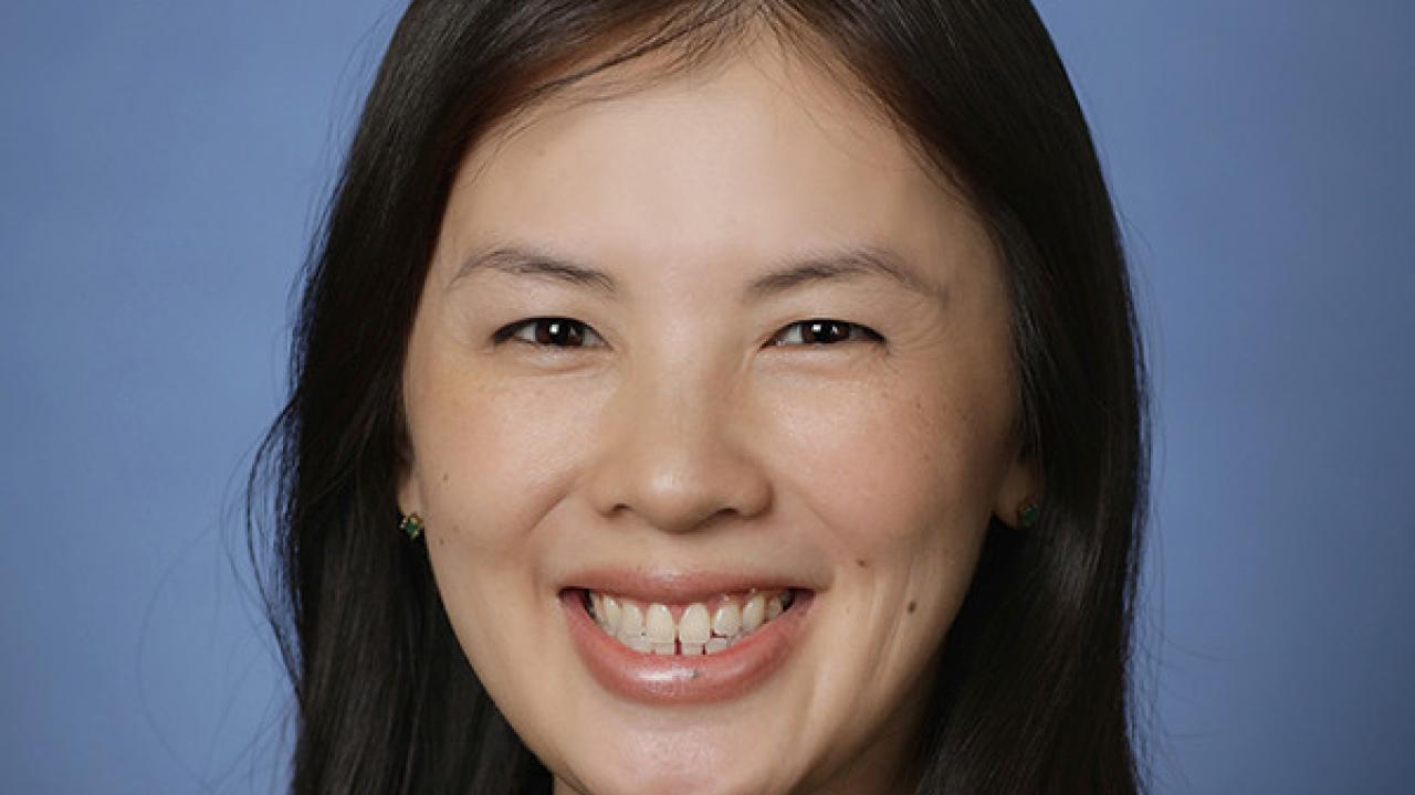 The picture shows a lady smiling, wearing a black top.