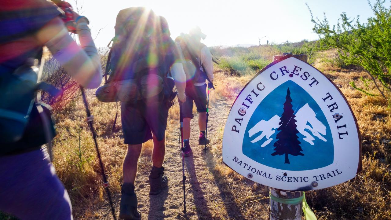 three hikers walking toward the sun next to a hiking trail sign