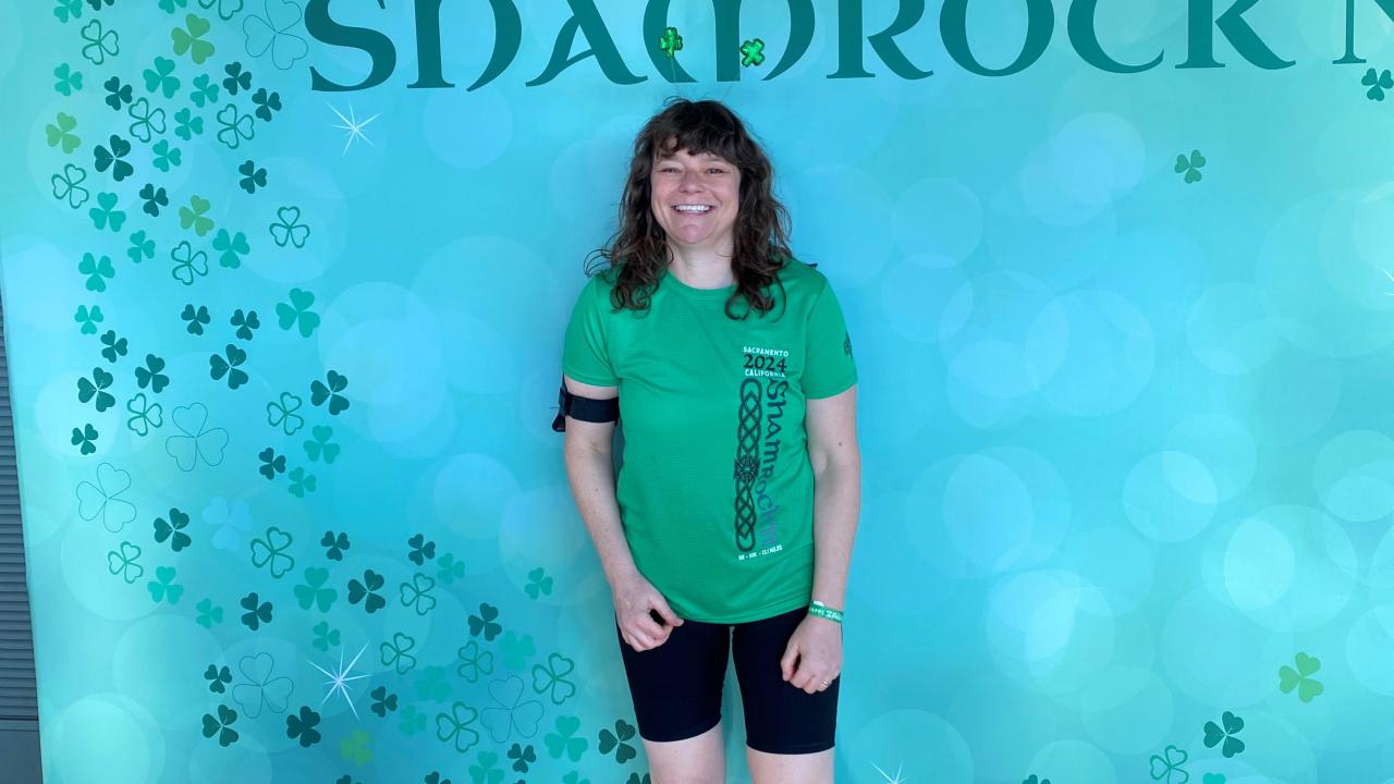 Becky Grunewald stands in front of a Shamrock n' Run poster