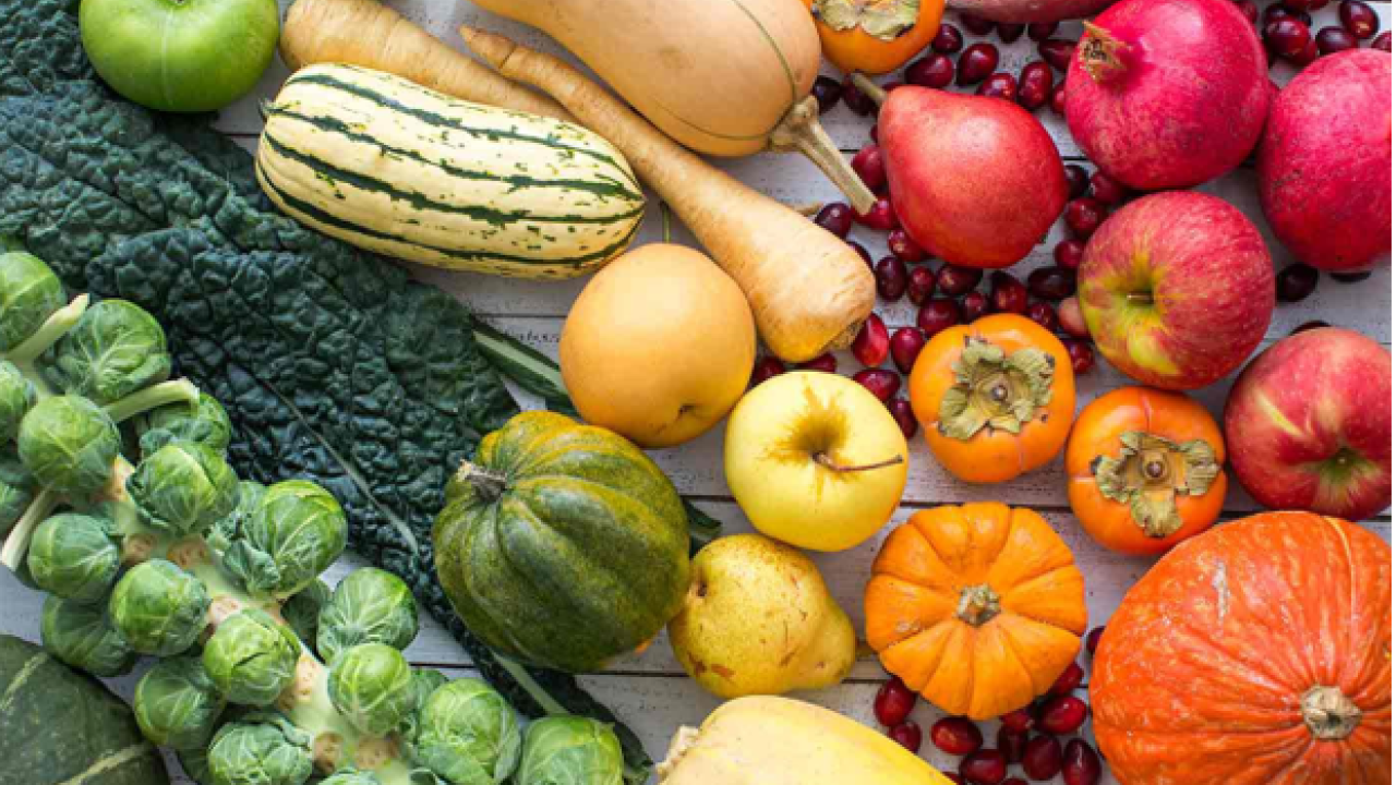 Assortment of fall fruits and vegetables ranging from green to red such as broccoli, squash, pumpkins, and apples.
