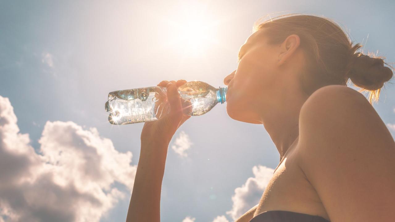 someone drinks water out of a water bottle on a hot summer day