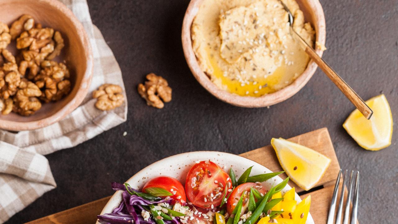 image of a colorful salad next to a bowl of hummus and a bowl of walnuts