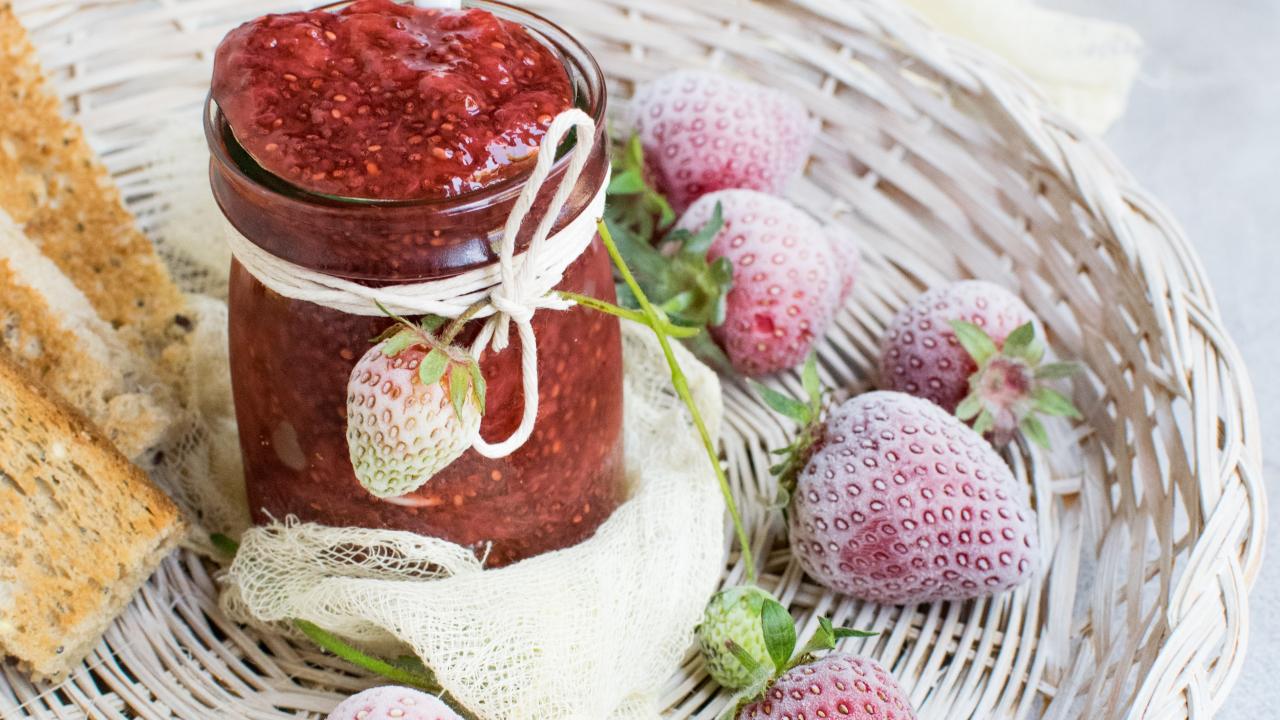 jar of strawberry jam and frozen strawberries on a white plate