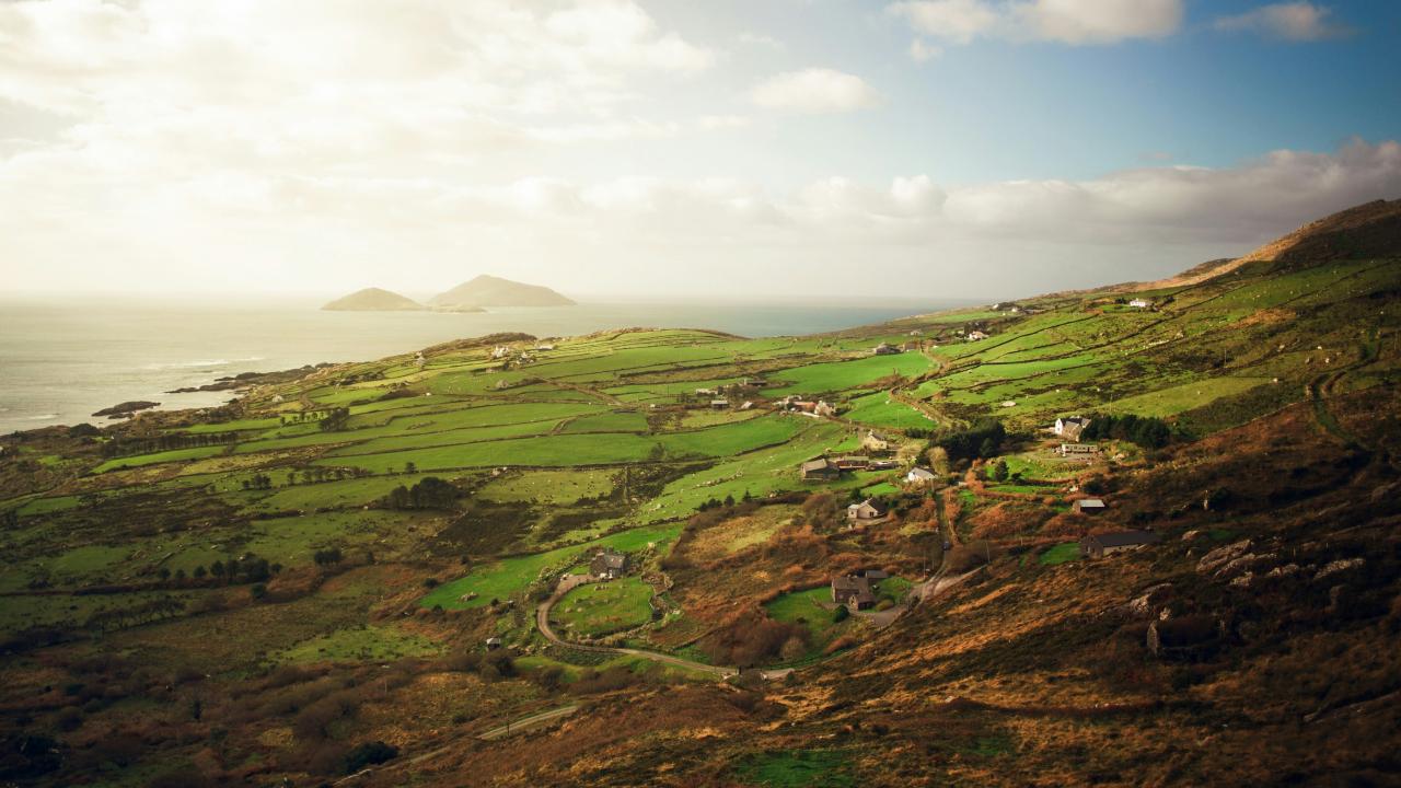 Image of green hillside and country homes in Ireland with the ocean in the background
