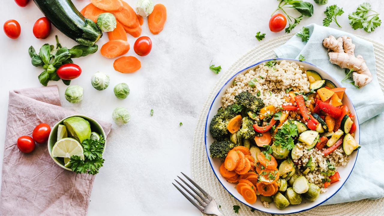 A bowl of vegetable salad surrounded by cucumbers, tomatoes, and carrots