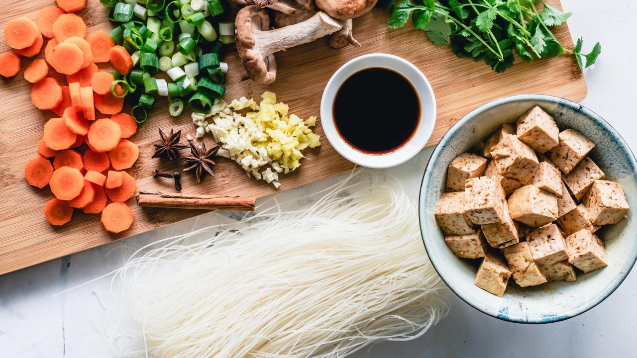 tofu and various vegetables prepared on a cutting board with a side of soy sauce