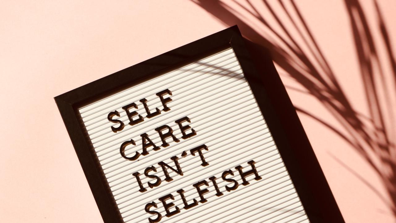 "Self Care isn't selfish" displayed on a board with a peach background