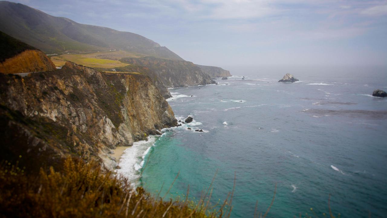 Image of a cliff along the ocean with rocks and small waves