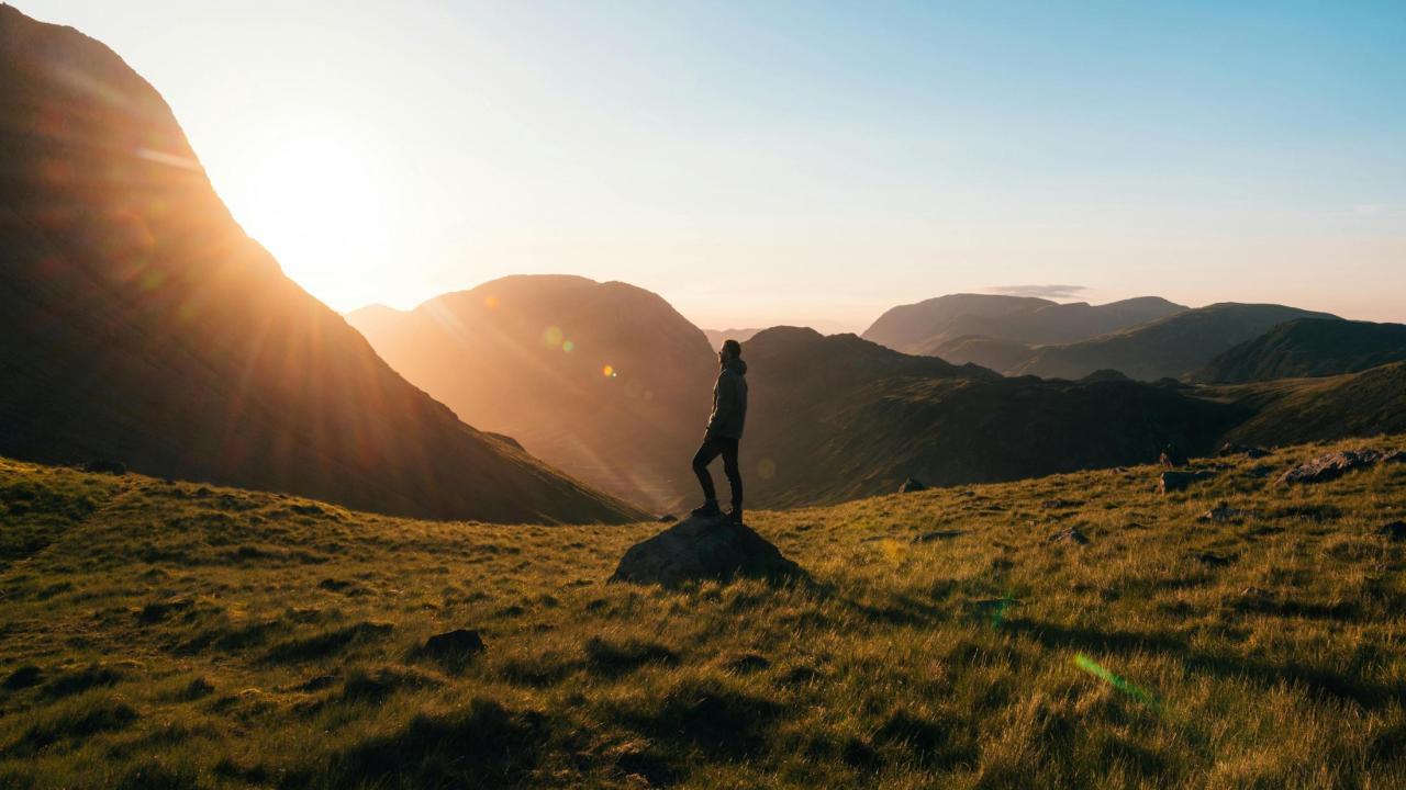 A person standing on the hiking trail with the sunset in the background.