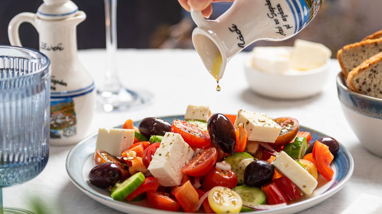 plate of feta tomato salad and person drizzling olive oil on top