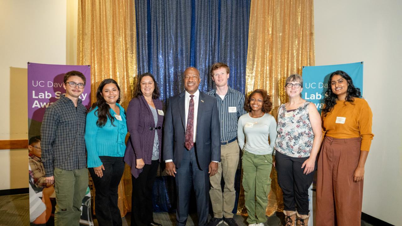 plant sciences lab team poses with chancellor with blue and gold sequins and safety posters