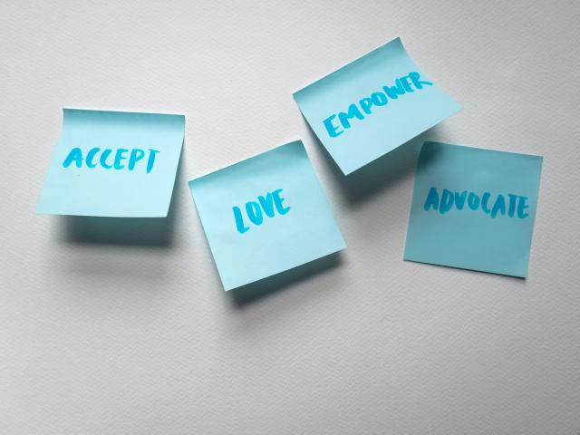 four blue sticky notes on a wall with the words, Accept, Love, Empower, and Change written on them