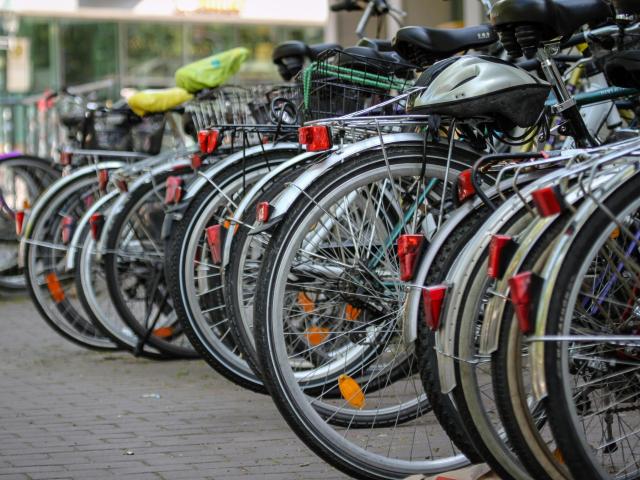 Row of parked bicycles with rear reflectors along a paved city sidewalk.