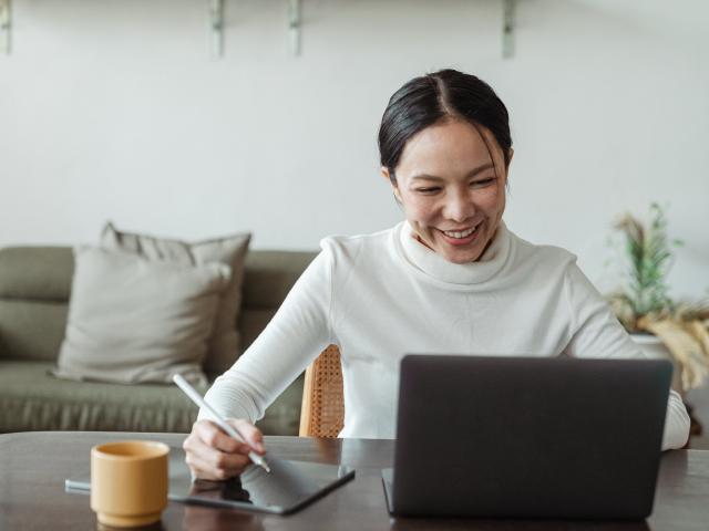 woman smiling at laptop taking notes