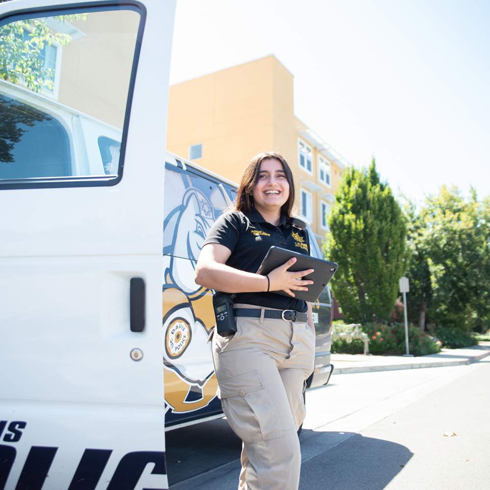 A female police officer stands in front of a UC Davis Police vehicle.