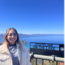Mayra stands in front of a sea line smiling