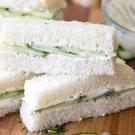 slice of sandwich on white bread with spread of cream cheese and cucumber inside on a wooden countertop