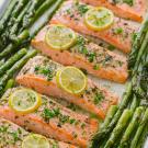 sheet pan with salmon filets topped with green herbs and lemon slices with asparagus lined up on each side
