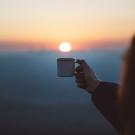 someone holding a mug under the setting sun in the background
