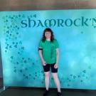 Becky Grunewald stands in front of a Shamrock n' Run poster