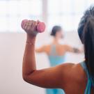 person holding a pink dumbbell with a 90 degree elbow in a fitness class