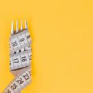 measuring tape wrapped around fork against yellow background